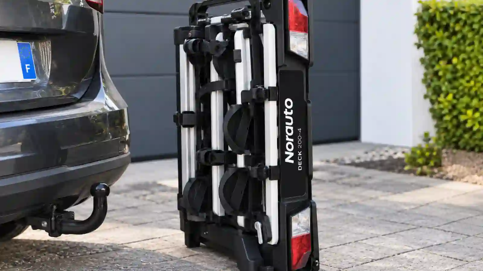 Porte-vélos Norauto DECK plié à côté d’une voiture avec attelage